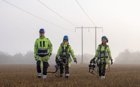 Tre medarbetare som går mot en Ledningsstolpe en dimmig dag.