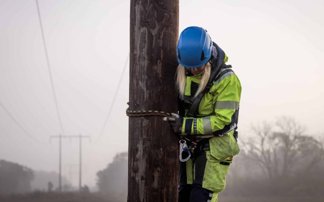 Medarbetare som klättrar i en stolpe ute i en ledningsgata.