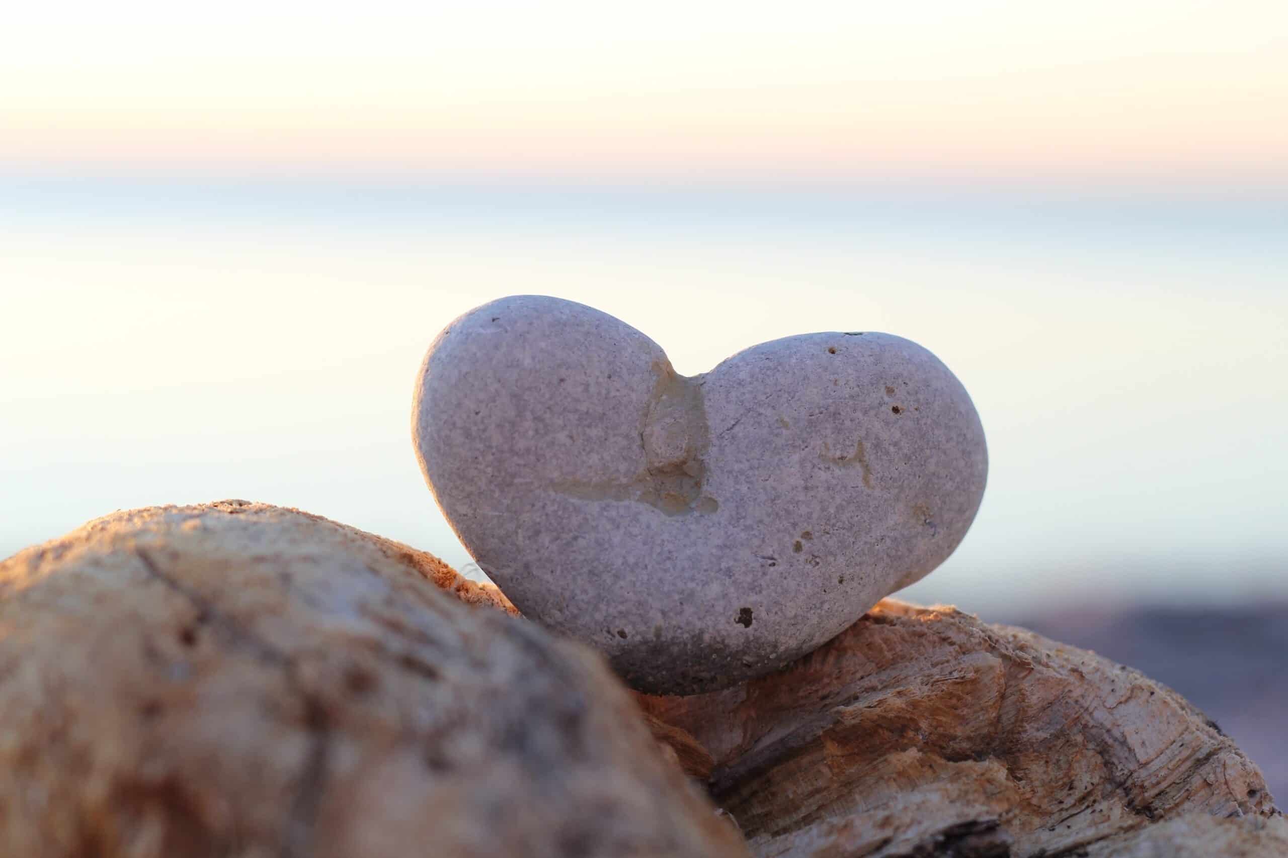 Hjärtformatisk sten på strand vid solnedgång eller soluppgång.