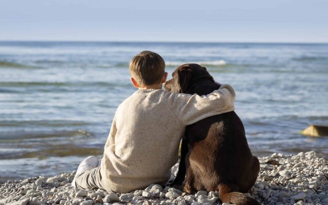 Barn som håller om en hund vid havet