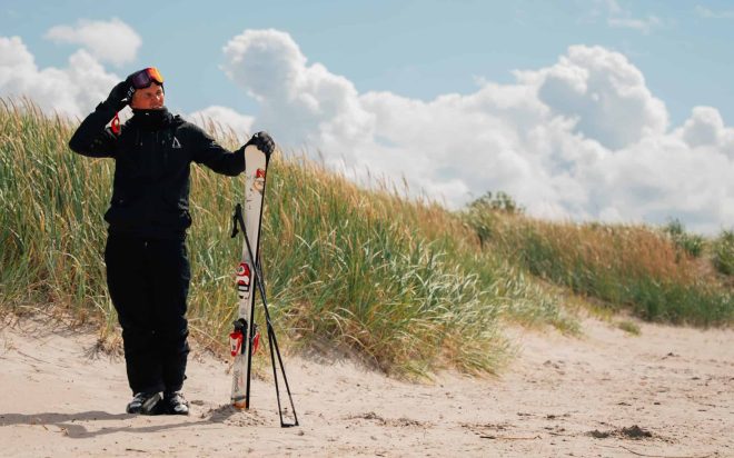 Person med skidutrustning på stranden en solig sommardag.